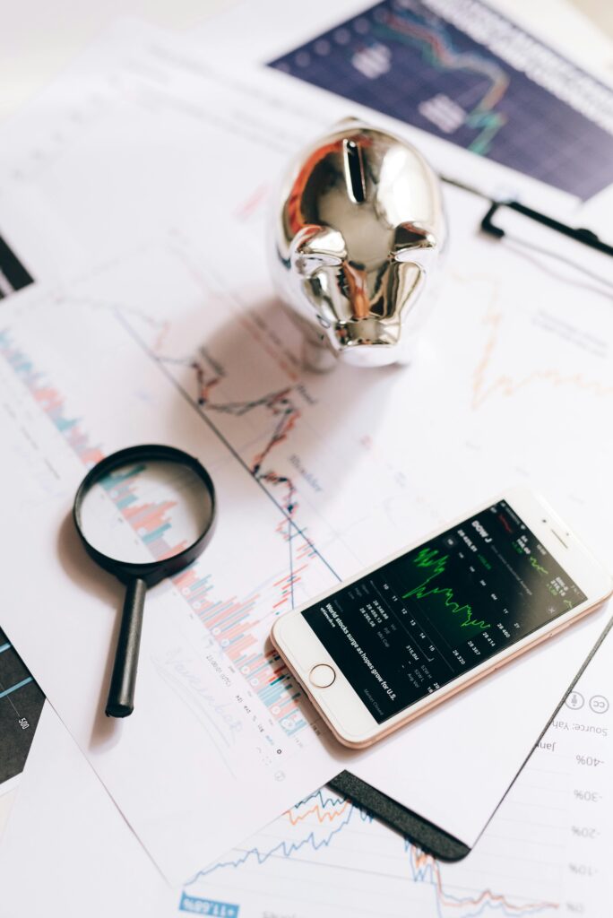 pexels-photo-5562086-5562086 Smartphone displaying stock market, piggy bank, and magnifying glass on financial charts.