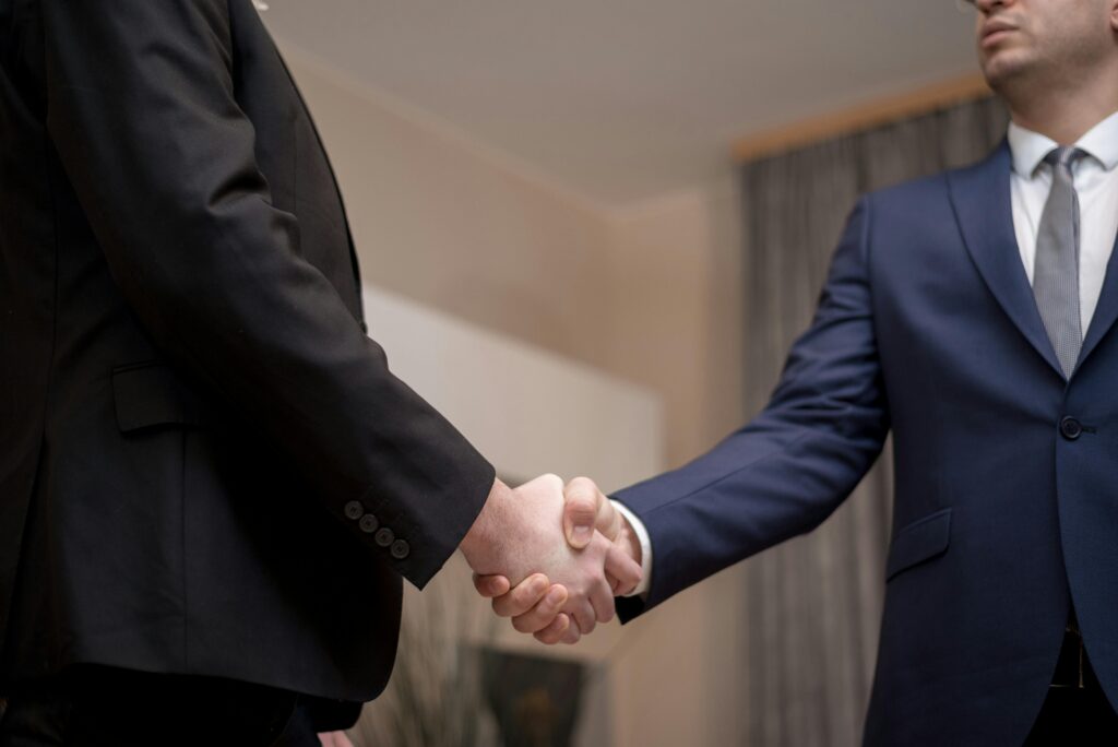 pexels-photo-6918507-6918507 Two businessmen in suits shaking hands, emphasizing trust and partnership indoors.